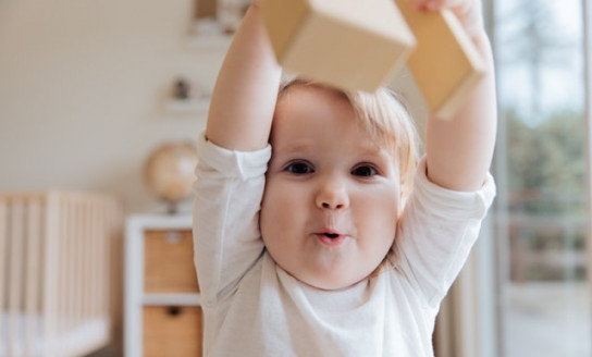 baby in white onesie holding wooden blocks 3933250