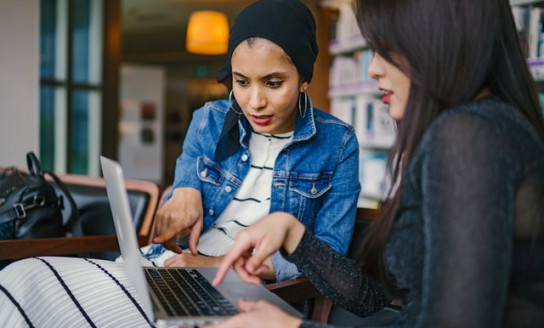 two women looking and pointing at macbook laptop 1569076