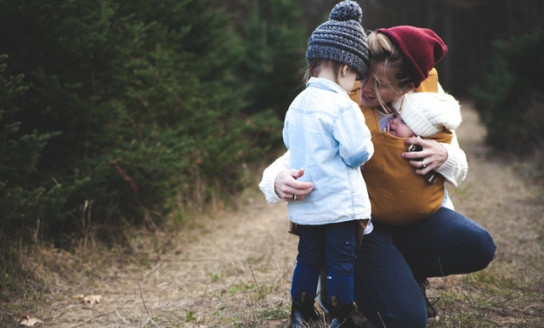 woman with brown baby carrier and little kid in white jacket 701014